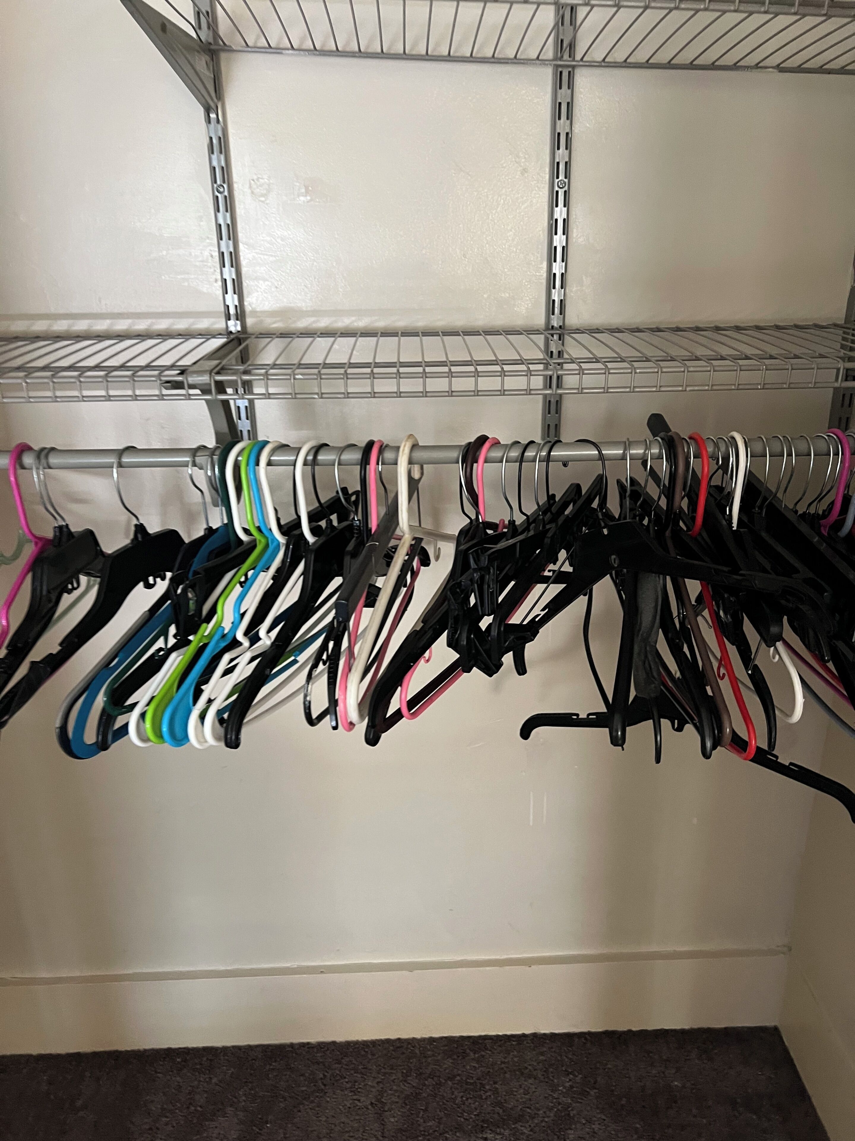 Un présentoir métallique avec plusieurs cintres de différentes couleurs, adossé à un mur.