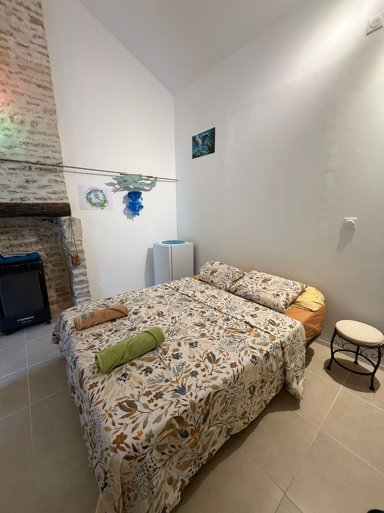 Ein Schlafzimmer mit einem Bett, einem kleinen Tisch, einem Heizgerät und einem an der Wand befestigten Bild.