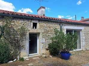 A stone building with a red-tiled roof, a small entrance, and a potted plant. - Studio Zen- Éco Hameau au porte du marais poitevin (Liez)