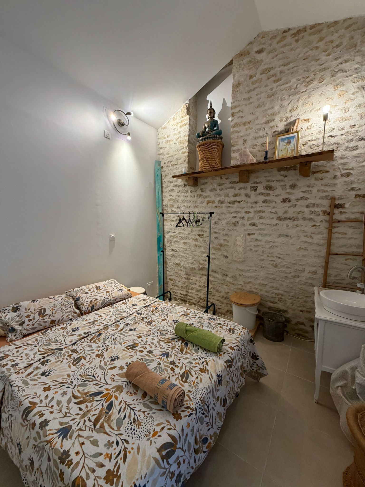 Une chambre à coucher avec un lit, une lampe suspendue, une statue de Bouddha et une salle de bain avec un lavabo et un miroir.