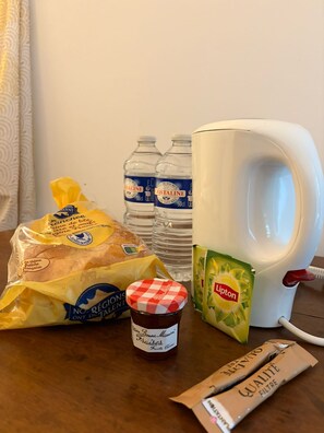 A table with a bag of bread, two bottles of water, a mug, a jar of jam, a packet of Lipton tea, and a box of quality filter coffee. - Studio Zen- Éco Hameau au porte du marais poitevin (Liez)