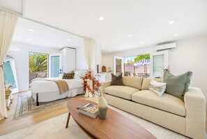 A modern hotel room with a bed, a sofa, a coffee table, and a view of the outdoors. - Coastal Casita, Stylish Beach Vacation (San Diego)