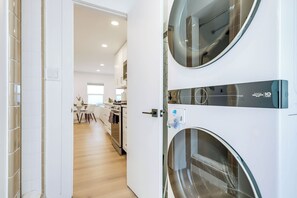 Een moderne wasruimte met twee voorladers, een houten vloer en uitzicht op een keuken.