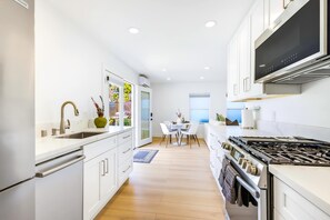 A modern kitchen with white cabinetry, a built-in stove, and a dining area with a table and chairs. - Coastal Casita, Stylish Beach Vacation (San Diego)