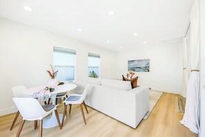 A modern living room with a white sofa, a dining table with chairs, and a painting on the wall. - Coastal Casita, Stylish Beach Vacation (San Diego)