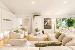 Un salón espacioso con un conjunto de sofá blanco, una mesa de centro y un mueble con adornos.