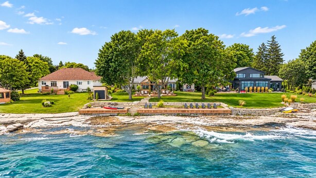 A coastal property with a rocky shoreline, a swimming area, and multiple houses with a well-maintained lawn and trees. - Lakehouse 99 - Tranquil Waterfront Getaway in the heart of Prince Edward County (Prince Edward)