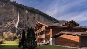 Un chalet in legno con un balcone, sullo sfondo di montagne e una cascata.