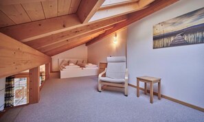 A loft bedroom with a sloped ceiling, a bed, a chair, a small table, and a painting on the wall. - SPACIOUS CHALET PENTHOUSE WITH SPECTACULAR MOUNTAIN VIEWS (Lauterbrunnen)