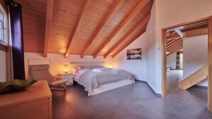 Una camera da letto con soffitto spiovente, un letto, comodini, una sedia e un quadro appeso al muro.