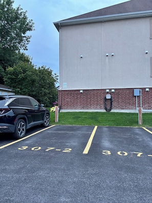 A parking lot with marked spaces, a building with a brick lower section, and a black car parked. - Condo in the National Capital (Gatineau)