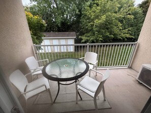A balcony with a glass table and white chairs, overlooking a grassy area and trees. - Condo in the National Capital (Gatineau)