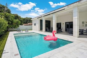 A swimming pool with a pink flamingo float, surrounded by a covered patio area with chairs and tables. - Casa Azure Family Friendly Home with Heated Pool (Miami)