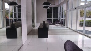 A spacious lobby with a modern design, featuring a reception desk, seating area, and large windows offering views of the outdoors. - Ilha Pura - flat Barra, security, comfort and a beautiful park at your disposal. (Rio de Janeiro)