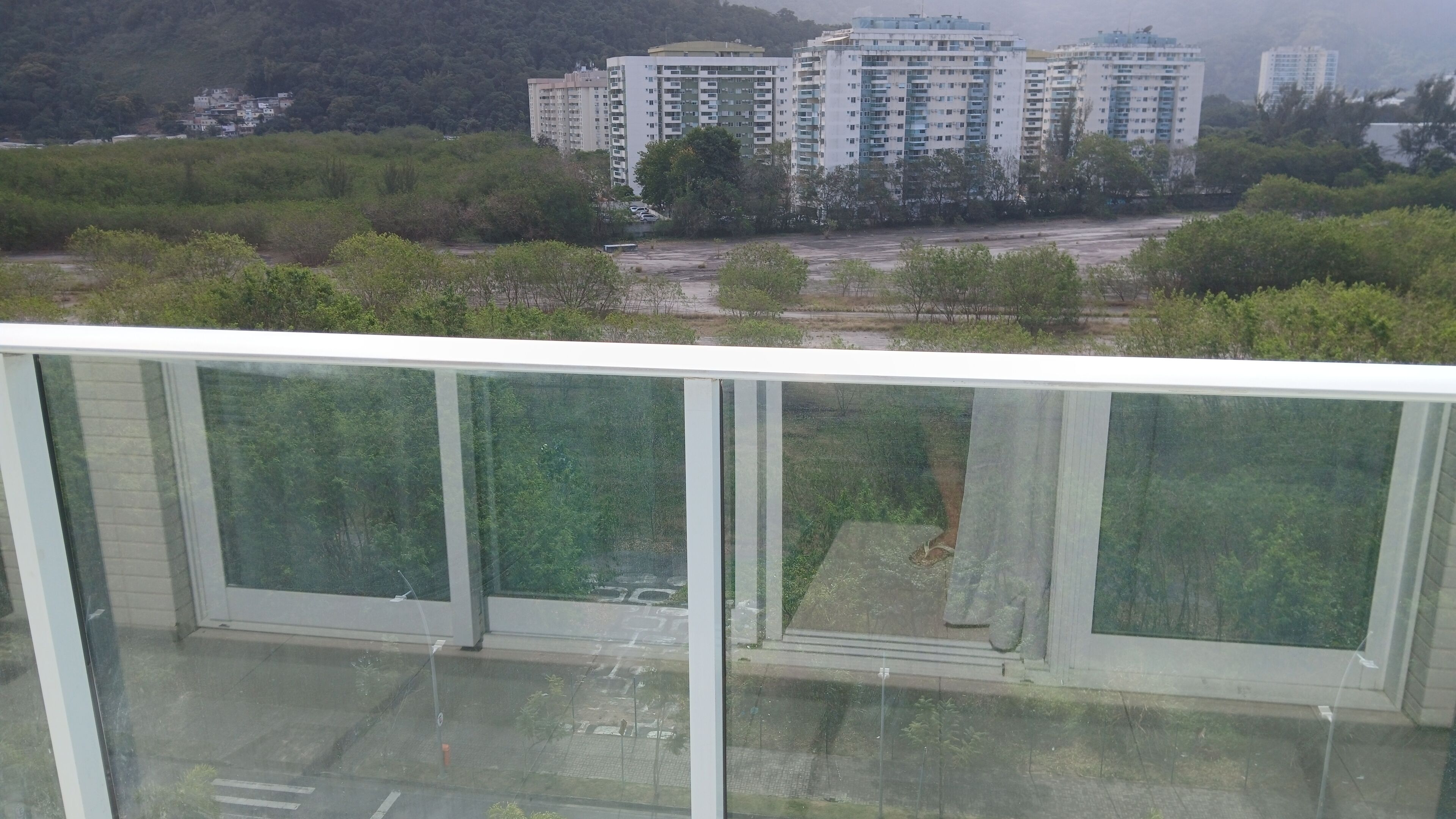 Blick von einem Balkon mit Glasgeländer auf einen Parkplatz und eine Reihe hoher Gebäude.