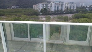 A view from a balcony with a glass railing, overlooking a parking area and a row of high-rise buildings. - Ilha Pura - flat Barra, security, comfort and a beautiful park at your disposal. (Rio de Janeiro)