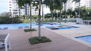 A pool area with lounge chairs, palm trees, and a tiled deck. - Ilha Pura - flat Barra, security, comfort and a beautiful park at your disposal. (Rio de Janeiro)