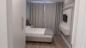 Un dormitorio con una cama, una mesita de noche, una lámpara, un televisor y una cortina.
