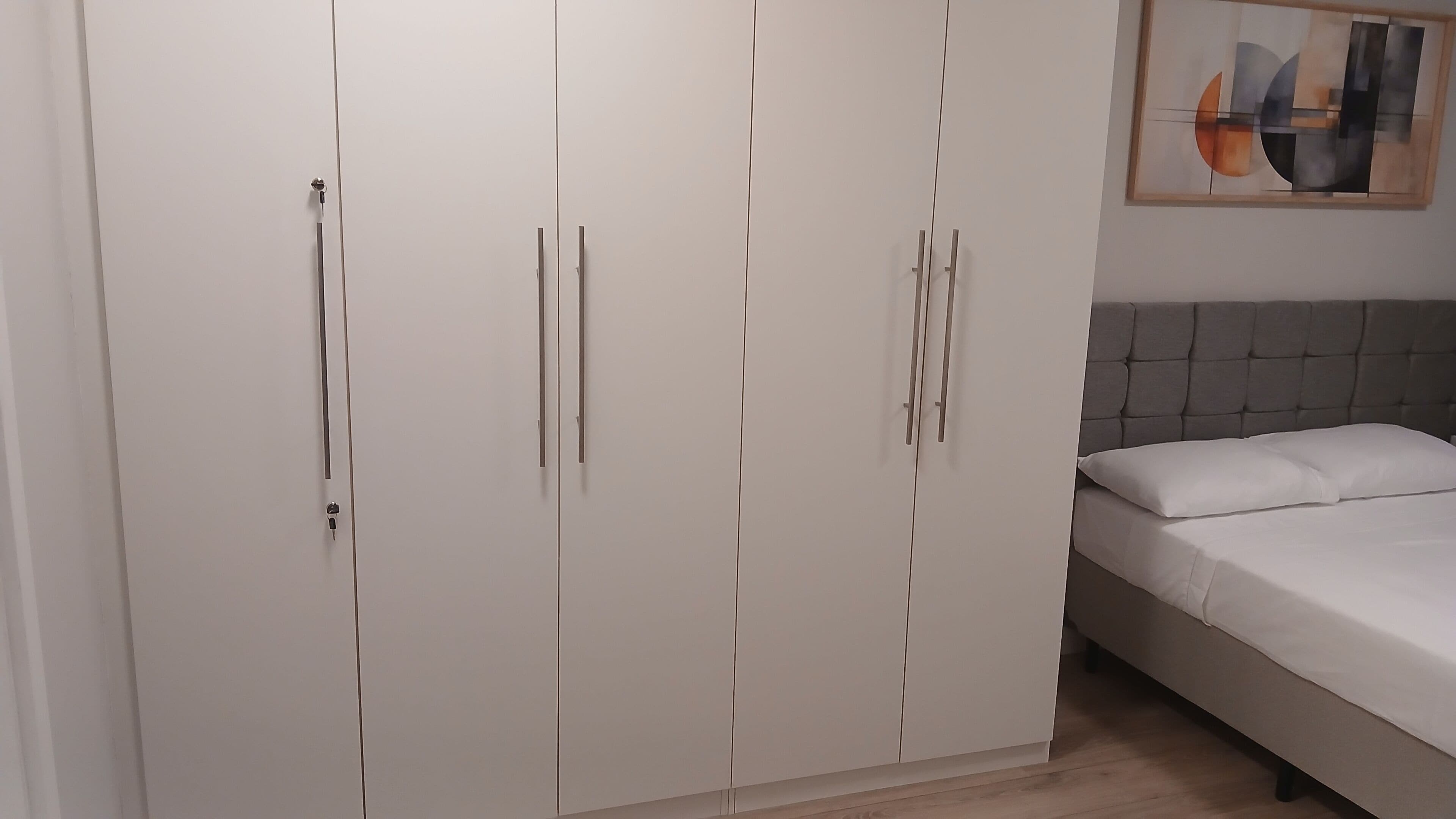 A bedroom with a bed, a wardrobe, and a painting on the wall.