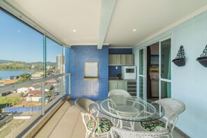A balcony with a glass table and chairs, a view of the city, and a kitchen area. - Breathtaking ocean views in Porto Belo. (Porto Belo)