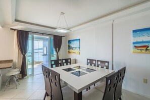 A dining area with a white table and dark chairs, a ceiling light, and a view through a glass door to the outside. - Breathtaking ocean views in Porto Belo. (Porto Belo)