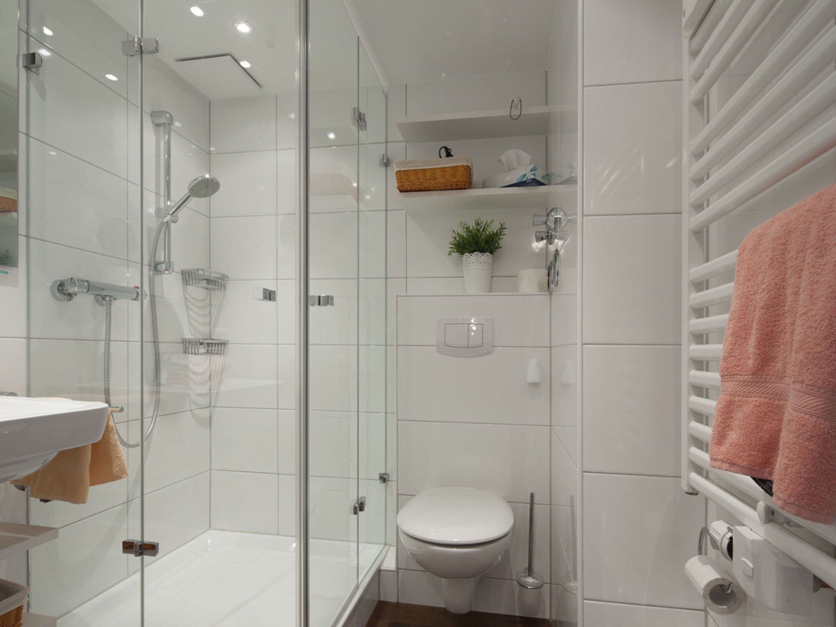 Un bagno moderno con doccia vetrata, un water bianco e un portascope con un asciugamano rosa.