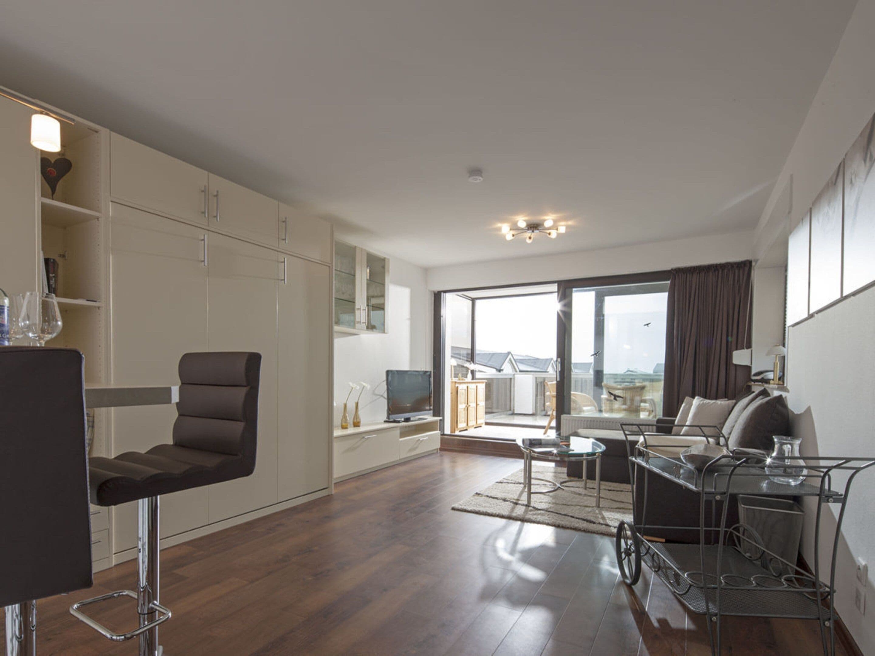 A modern living room with a sofa, a dining area with a bar stool, and a large window offering a view of the outdoors.