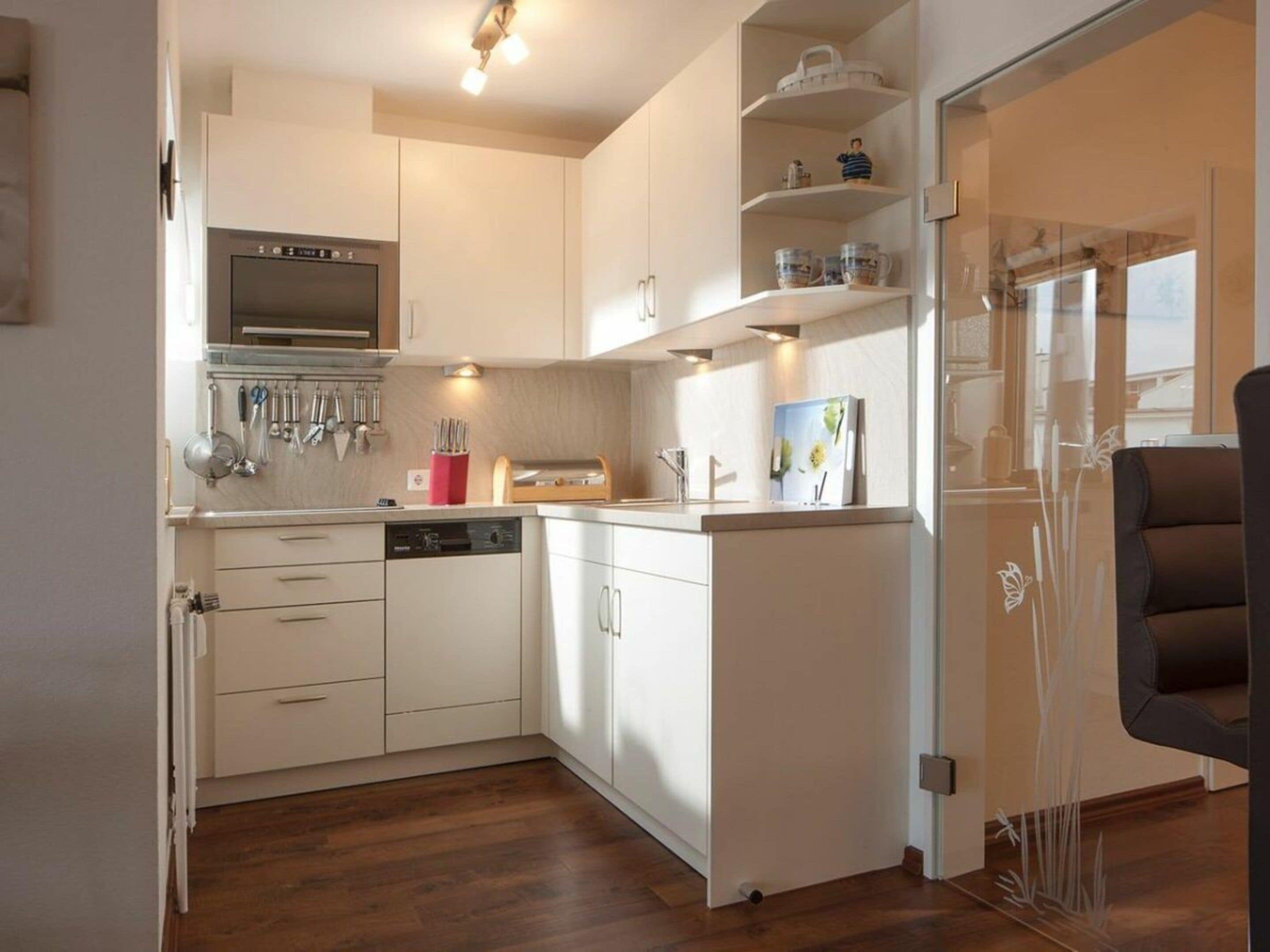 Een moderne keuken met witte kasten, een ingebouwde oven en een vaatwasser. Er is een eethoek met een zwarte stoel te zien.