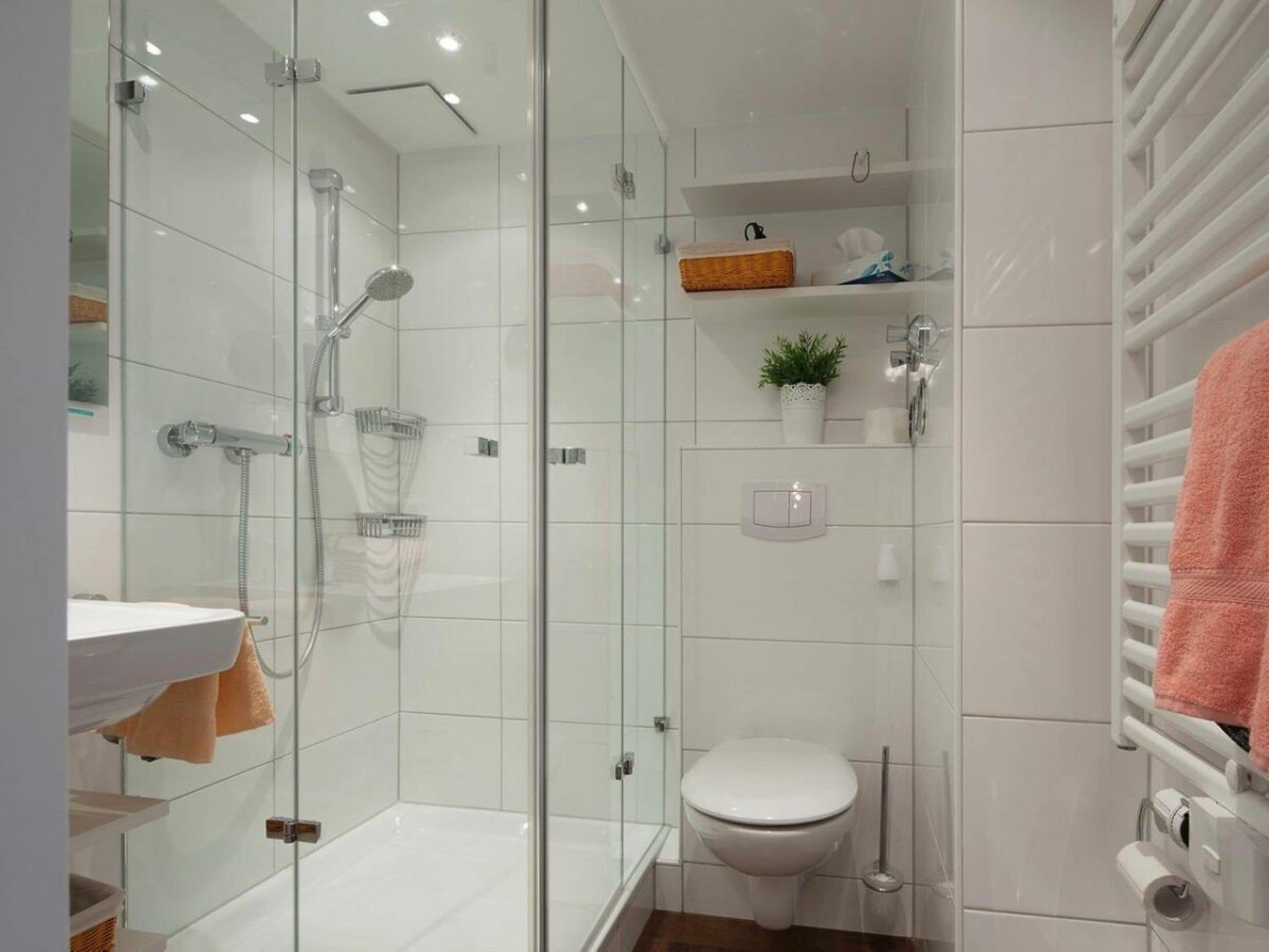 Uma casa de banho moderna com chuveiro em cabine de vidro, sanita branca e porta-toalhas com uma toalha cor-de-rosa.