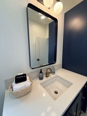 A bathroom with a white sink, a mirror, a towel rack with a towel, a soap dispenser, and a bottle of liquid soap.
