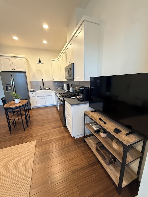 A modern kitchen with white cabinets, a stainless steel refrigerator, a microwave, and a large flat-screen TV.