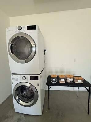 A stacked washer and dryer unit with a table beside it holding laundry supplies.
