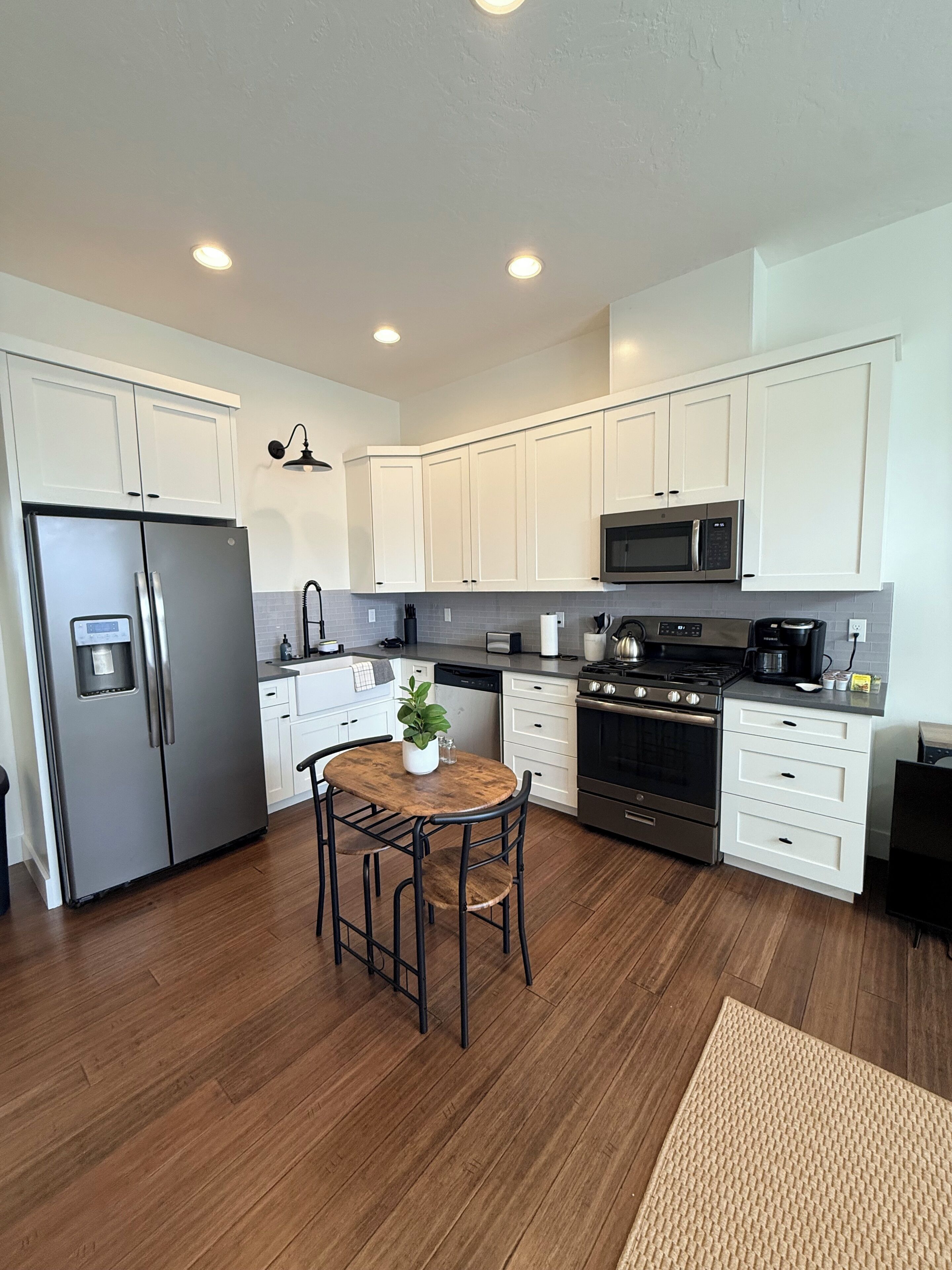 A modern kitchen with white cabinets, stainless steel appliances, and a wooden dining table with chairs.