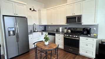 A modern kitchen with white cabinets, stainless steel appliances, and a wooden dining table with chairs.
