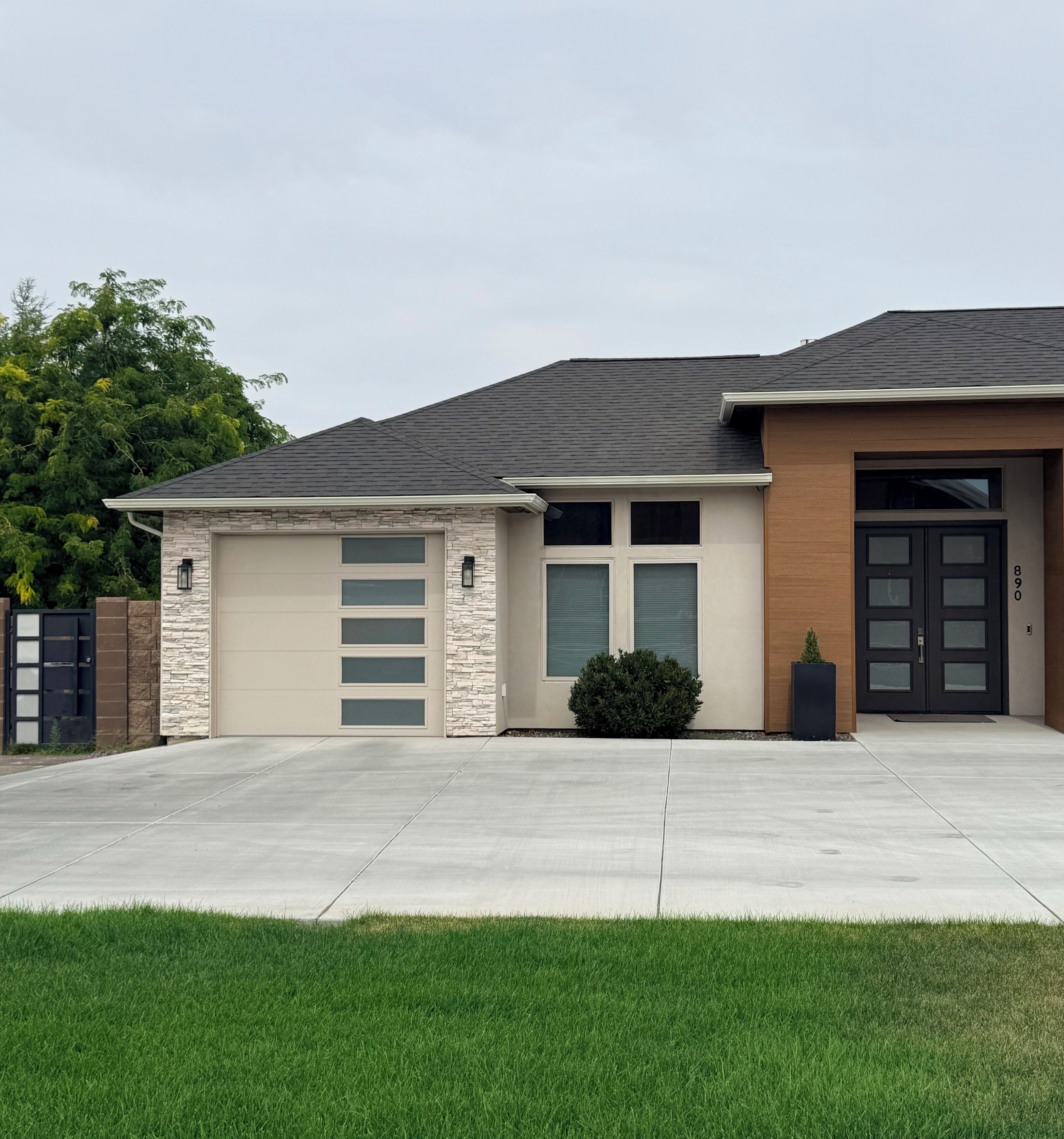 A modern two-story house with a garage, a stone facade, and a well-maintained lawn.