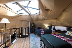 Acomodação em tenda com claraboia, cama, escrivaninha, ventilador e escada.