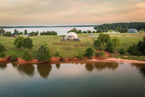 Uma propriedade à beira do lago com uma grande estrutura em forma de cúpula, um campo gramado e uma extensão de água.