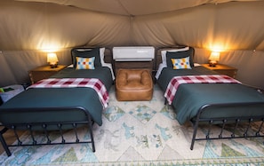 A tented room with two beds, a central bench, and a ceiling-mounted air conditioning unit.