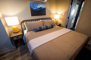 Ein ordentlich bezogenes Bett mit einer gestreiften Decke, zwei Nachttischlampen und einem Nachttisch mit einer Lampe.