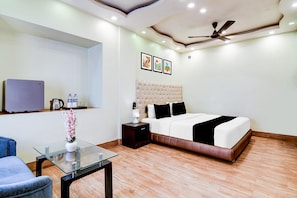 A hotel room with a bed, a glass table, a chair, a ceiling fan, and artwork on the wall.