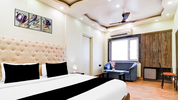 A hotel room with a large bed, a sofa, a desk, and a wardrobe. - Deluxe Room Aspiring Inn (Kolkata)