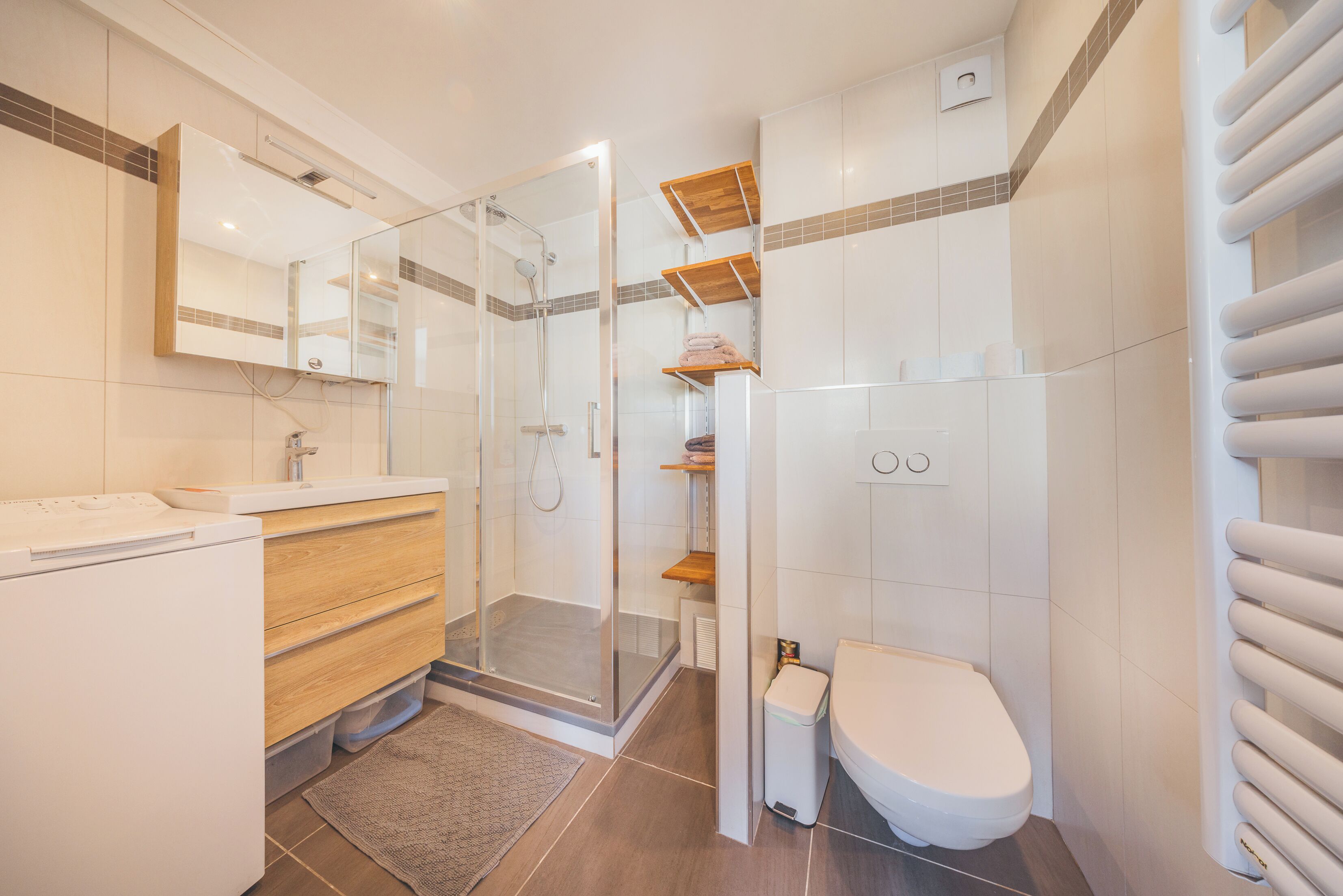 A modern bathroom with a glass-enclosed shower, a wooden vanity, a toilet, and a towel rack.