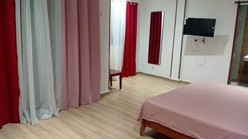 Een slaapkamer met een bed, een houten vloer, een aan de muur bevestigde televisie en rode gordijnen.