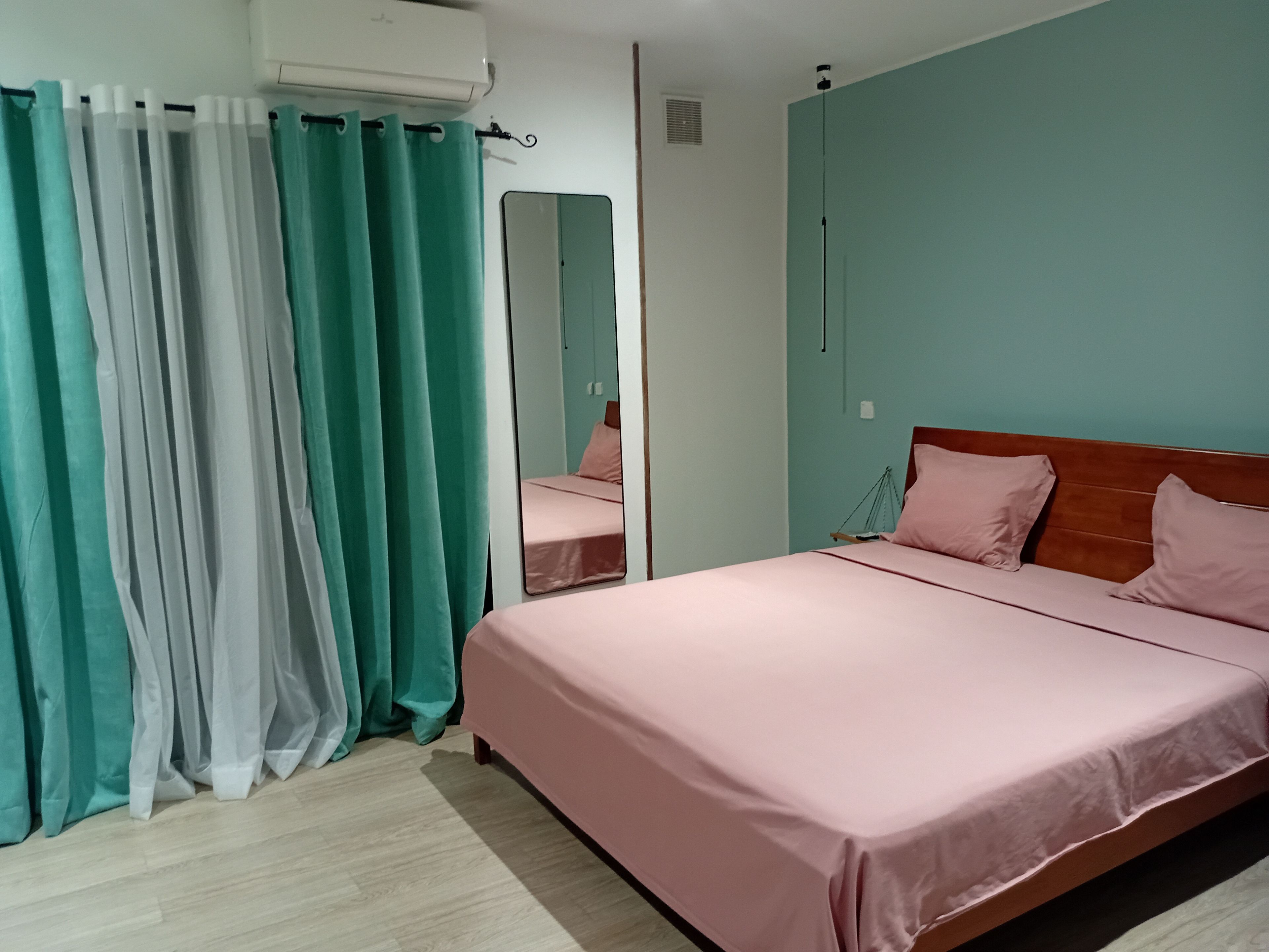 A bedroom with a bed, curtains, a mirror, and a wall-mounted air conditioner.
