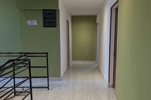A hallway with a metal staircase on the left, a green wall, and a tiled floor.