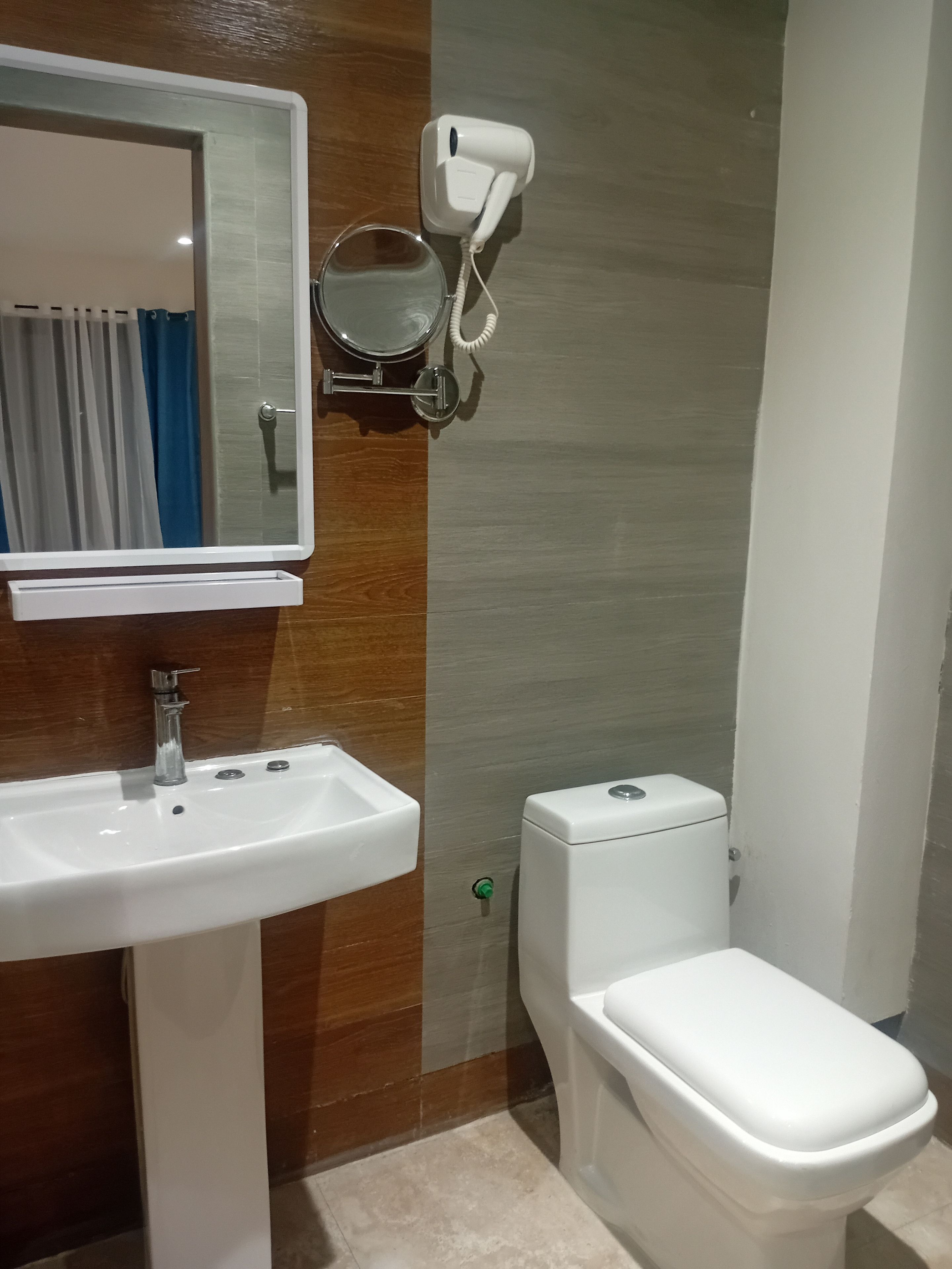 Un baño con un lavamanos blanco, un espejo, un inodoro y un secador de pelo montado en la pared.