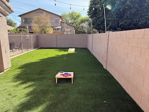 Ein Garten mit Kunstgrasanlage, einem Holztisch und einer Ziegelwand.