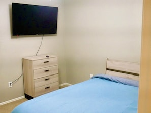 Ein Schlafzimmer mit einem Bett, einer Kommode und einem an der Wand befestigten Fernseher.