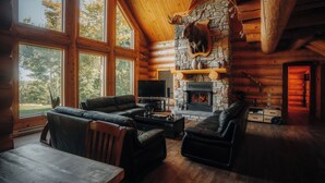 A log cabin interior with a stone fireplace, leather sofas, and a television.