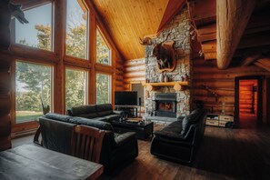 A log cabin interior with a stone fireplace, leather sofas, and a television. - Luxury log cabin 1 hour from Montreal (Mille-Isles)